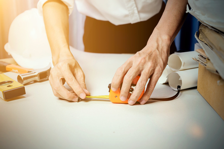 Business man working in his job, young man engineer measuring something on his construction project for create a blueprint in the workplace, vintage tone with sunlight effect photography.の写真素材