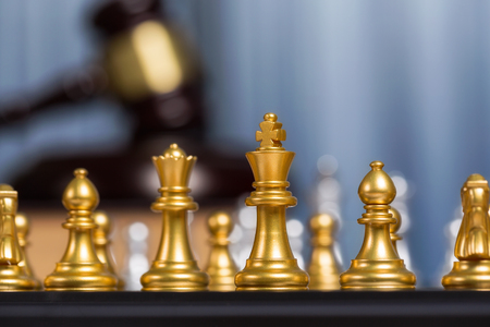 Close up golden king of chess or checkers with blurry gavel meaning fighting, justice and victory for lawyer job background.の写真素材
