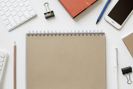 Blank notebook paper on office desk table with mobile, keyboard, tablet, pencil and other objects.の写真素材