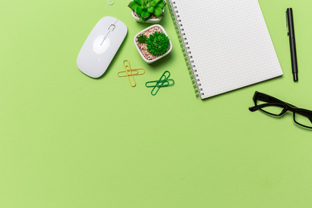 Green office desk table with grid note paper book, mouse, eye grasses, view from above in studio photography with copy space. Flat lay.の写真素材