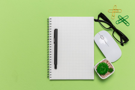 Green office desk table with grid note paper book, mouse, eye grasses, view from above in studio photography with copy space. Flat lay.の写真素材