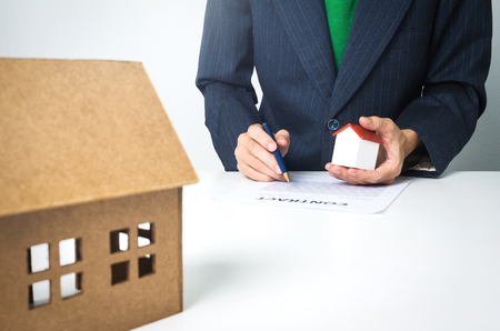 Real estate insurance lawyer working hard job, signing a contract with wooden house model.の写真素材
