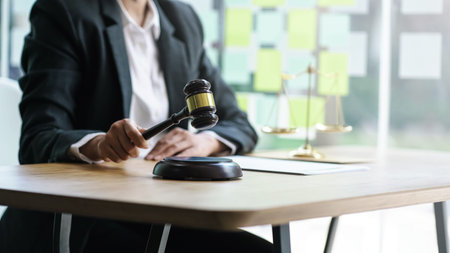 Young woman lawyer holding wooden gavel with blurry golden scales.
