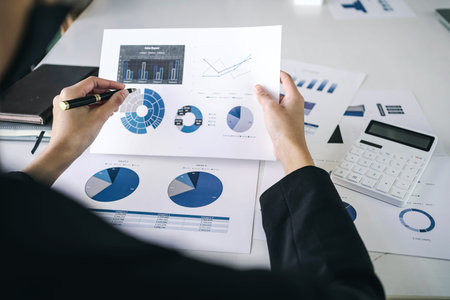 Rear view of business woman analysis financial chart data and graph, close up at hand holding pen.