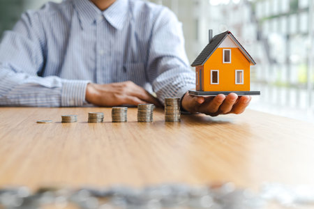 Business man holding house toy with stack of coin, saving money for buy a new house concept.