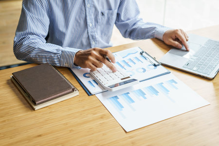 Close up hands of business man using a calculator to calculate expenses from receipts placed on the...