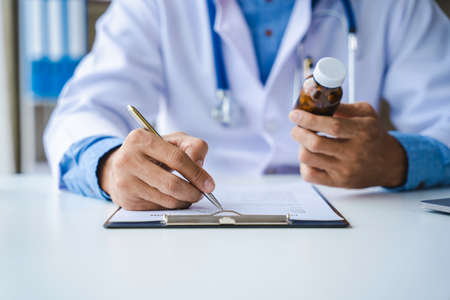 Close-up of doctor's hands writing prescription and holding bottle with pills. Healthcare, medical and pharmacy concept.の写真素材