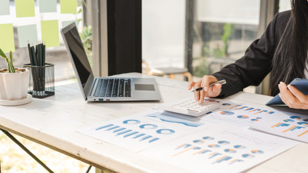 Close up Business woman using calculator to do math finance on wooden desk in office and analysis data the charts and graphs at desk.の写真素材