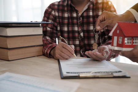 Give a house key, Credit approver, businessman in male suit and house toy model mockup Home loan mortgage approval concept. After signing the contractの写真素材