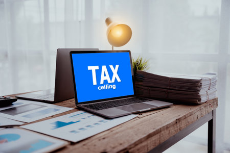 laptop with the word "TAX ceiling" on the screen, a lamp, and a stack of papers on a desk.の写真素材