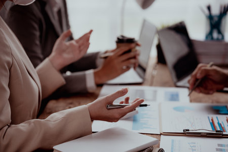 Business meeting with hands pointing at financial charts and a laptop on a wooden table.の写真素材
