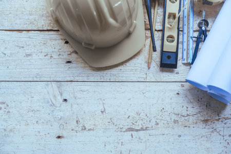 Top view construction tools such as a yellow hard hat, spirit level, measuring tape, folding ruler arrayed against a wooden plank background.の写真素材