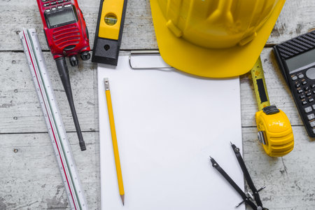 Top view construction tools such as a yellow hard hat, spirit level, measuring tape, folding ruler arrayed against a wooden plank background.の写真素材