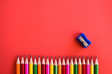 Colorful pensils align in a row shot  with a sharpener on a plain isolated red background as wallpaper.の写真素材