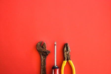Screwdriver, rusty adjustable spanner and pliers shot on a plain isolated red background as wallpaper.の写真素材