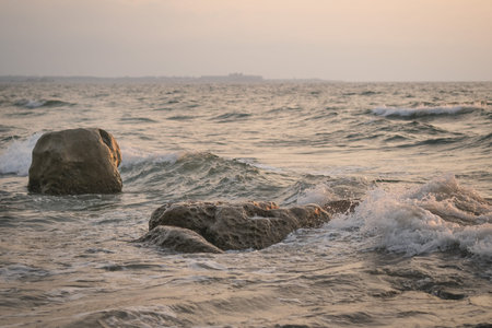 Seawaves hitting rocks on beach during sunset.
