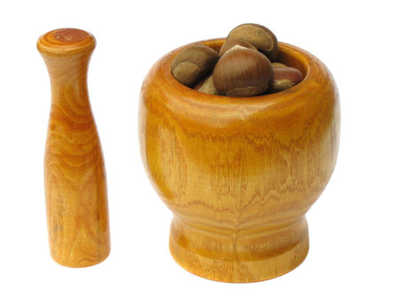 Wooden  mortar with pestle standing near by with chestnuts inside the bowl on white background