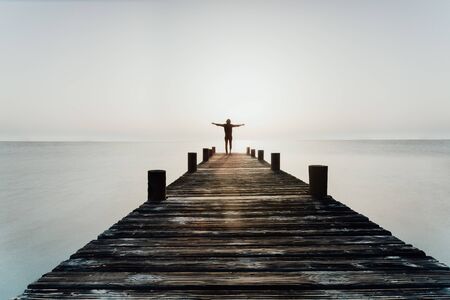 Person stands with open arms at sunrise on the jettyの写真素材