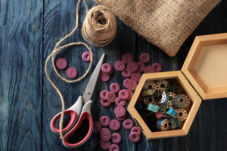 Accessories for sewing and needlework. a casket with bobbins, buttons, scissors and burlap on a dark blue wooden background. top viewの写真素材