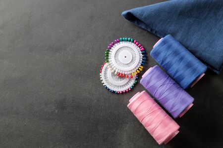Accessories for sewing a bobbin with thread, pins and a piece of cloth on a black background with a place for an inscription. top viewの写真素材