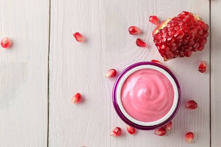 Cosmetic cream in a lilac jar and with fresh pomegranate on a white wooden table. pomegranate extract. cosmetics. top viewの写真素材