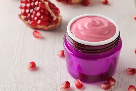 Cosmetic cream in a lilac jar and with fresh pomegranate on a white wooden table. pomegranate extract. cosmetics.の写真素材