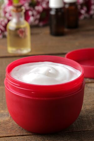 Cosmetic cream in a red jar close-up and flowers of chrysanthemum on a brown wooden table. cosmeticsの写真素材