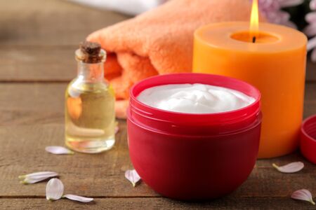 Cosmetic cream in a red jar of candle oil towel in the background on a brown wooden table. spa. relax. cosmeticsの写真素材