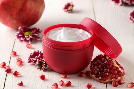 Cosmetic cream in a red jar with flowers and fresh pomegranate on a white wooden table. pomegranate extract. cosmetics.の写真素材