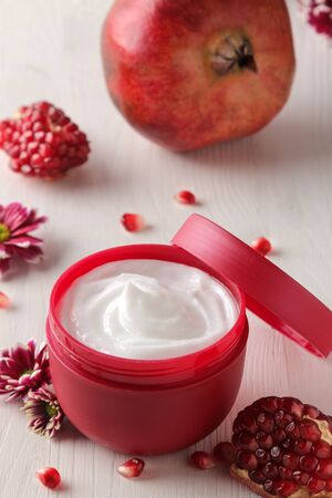 Cosmetic cream in a red jar with flowers and fresh pomegranate on a white wooden table. pomegranate extract. cosmetics.の写真素材
