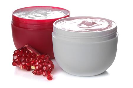 Cream in a white and red jar next to fresh pomegranate on a white isolated backgroundの写真素材