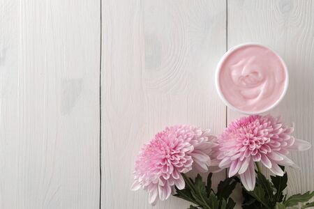 A cream in a jar and flowers of chrysanthemum on a white wooden table with a place for an inscription. cosmetics. top viewの写真素材