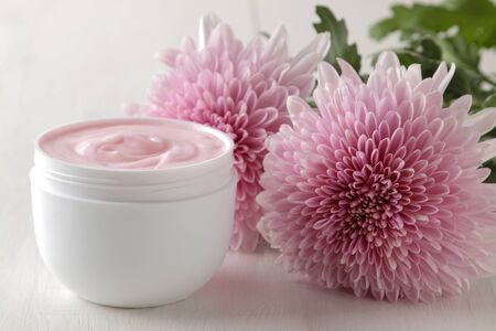 Cream in a white jar close-up and flowers of chrysanthemum on a white wooden table. cosmeticsの写真素材