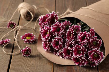 A large bouquet of autumn flowers of chrysanthemums in craft paper on a brown wooden tableの写真素材