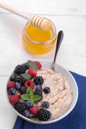 Oatmeal with berries and honey in a bowl on a white wooden table. breakfast. healthy food.の写真素材