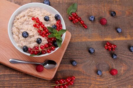 Oatmeal with berries in a bowl on a brown wooden table. breakfast. healthy food. top viewの写真素材