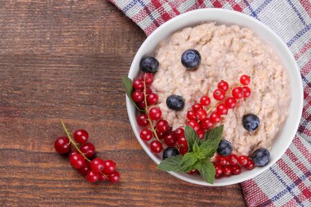 Oatmeal with berries in a bowl on a brown wooden table. breakfast. healthy food. top viewの写真素材