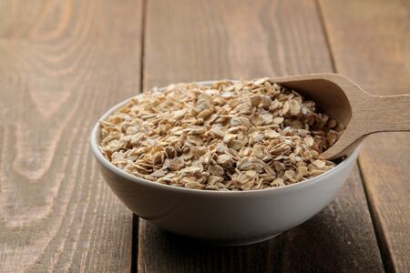 Dry oatmeal in a white bowl and a wooden spoon. food. healthy food. on a brown wooden table.の写真素材