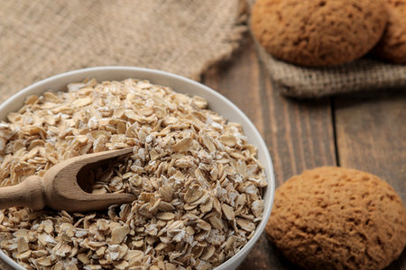 Dry oatmeal and oatmeal cookies in a white bowl and a wooden spoon. food. healthy food. on a brown...