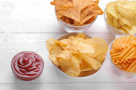 Different types of chips in bowls and red sauce on a white wooden table.の写真素材