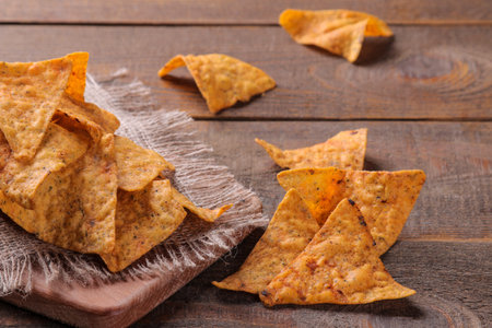 Chips. A lot of nachos on the board on a brown wooden table. unhealthy food