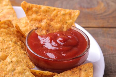 Chips. Nachos on a white plate with red sauce on a brown wooden background close-upの写真素材