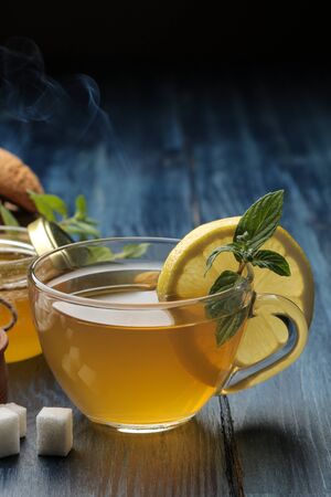 Hot green tea with cinnamon, mint and lemon next to sugar on a blue wooden tableの写真素材