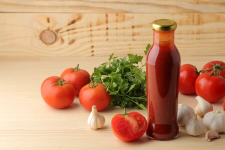 Red sauce in a bottle with fresh ingredients, tomatoes, pepper and garlic on a natural wooden background. With space for inscriptionsの写真素材