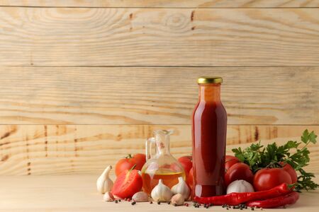 Red sauce in a bottle with fresh ingredients, tomatoes, pepper and garlic on a natural wooden background. With space for inscriptionsの写真素材