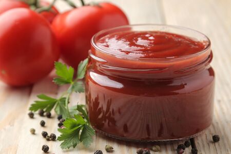 Red sauce in a jar close-up with fresh tomatoes on a natural wooden tableの写真素材