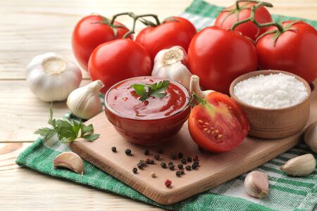 Red sauce in a bowl with fresh ingredients, tomatoes, garlic and spices on a natural wooden table.の写真素材