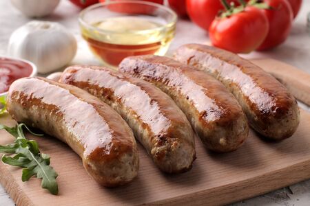 Grilled sausages with tomatoes, sunflower oil and garlic on a light backgroundの写真素材