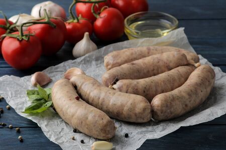 Raw sausages with ingredients for cooking tomatoes, garlic, butter and basil. on a blue wooden table.の写真素材