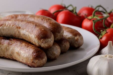 Grilled sausages with tomatoes, sunflower oil and garlic on a light backgroundの写真素材